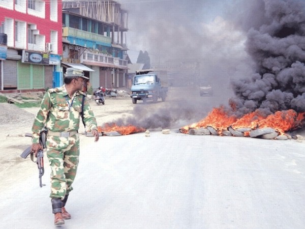 A security personnel walks pass a road in Imphal being blocked with burning of tyres