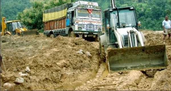 File: An excavator clearing the way for goods carriers on NH-37